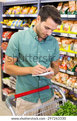 Serious man writing on list on his notepad at supermarket