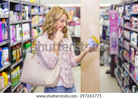 Side view of a pretty blonde woma looking at a product in supermarket