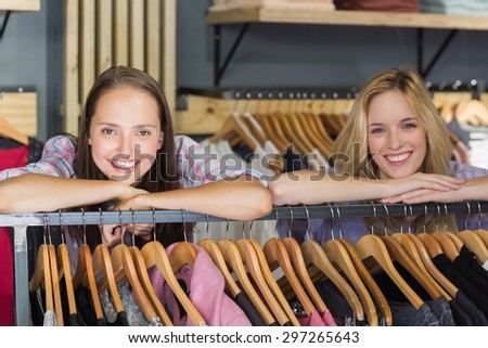 Two beautiful women with head on hand smiling at camera in clothes store