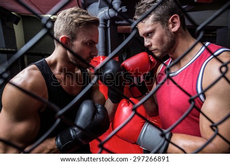 Side view of two determined boxing men behind the netting