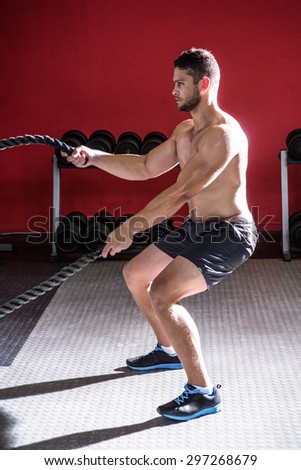 Muscular man exercising with rope in crossfit gym