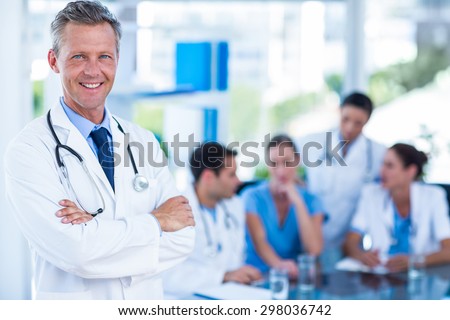 Doctor smiling at camera with colleagues behind in medical office