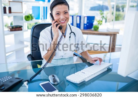 Smiling doctor having phone call and using her computer in medical office