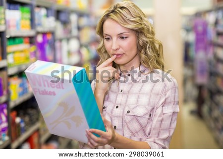 Smiling pretyt blonde woman reading on a box in a supermarket