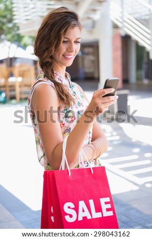 Smiling woman with sale shopping bags using smartphone at the shopping mall