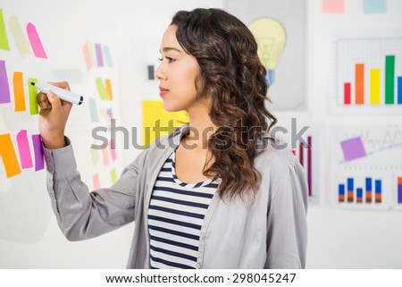Young serious businesswoman writing on sticky notes on the wall in the office
