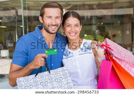 Young happy couple looking camera after shopping holding a credit card
