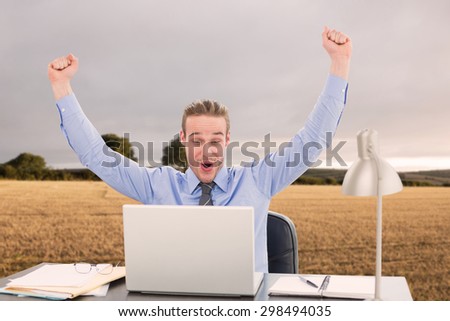 Cheering businessman at laptop against bright brown landscape