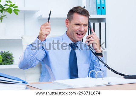 An angry businessman phoning at his desk in the office