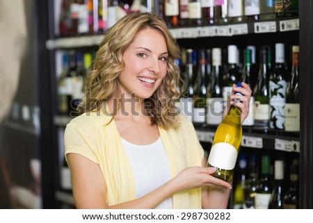 Portrait of a smiling pretty blonde woman showing a wine bottle in supermarket
