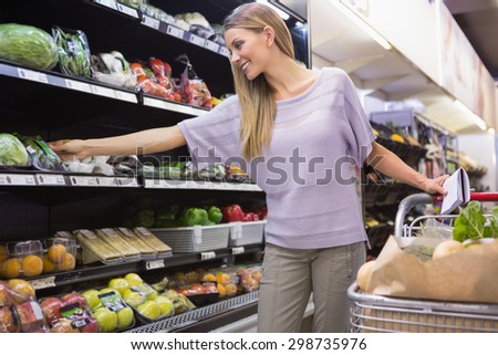 Smiling woman reading on his notepad in aisle at supermarket