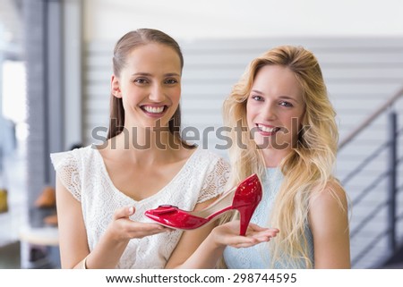 Happy women smiling at camera and showing a heel shoe in shoe store