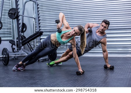 Portrait of a muscular couple doing side plank while lifting weights