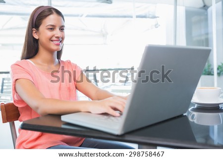 Young happy woman typing on the laptop in the cafe