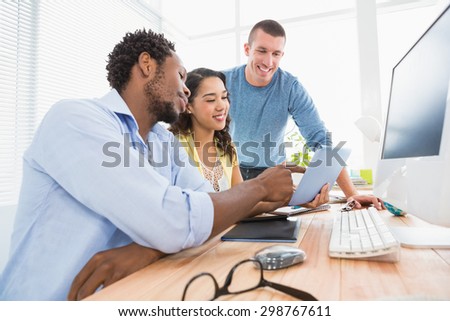 Smiling coworkers using tablet computer together and pointing the screen in the office