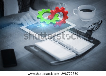 Green and red cog and wheel against creative businessman using a tablet