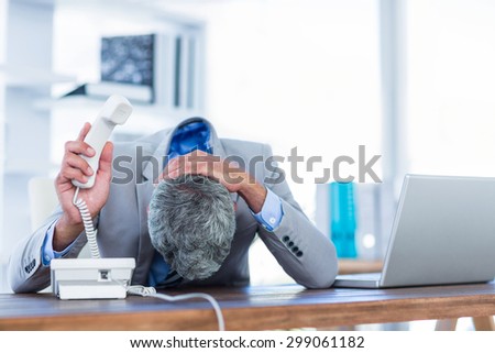 Depressed businessman holding phone in office