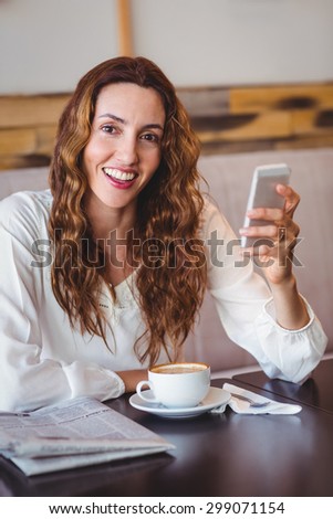 Woman using her mobile phone and holding cup of coffee at the coffee shop