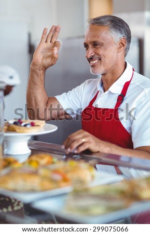 Happy barista gesturing ok sign behind counter in the bakery
