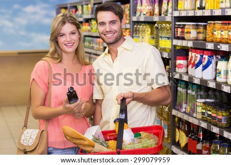 Portrait of smiling bright couple buying food products using shopping basket at supermarket