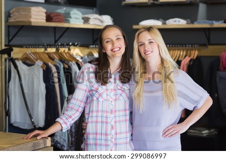 Two female friends standing together and smiling at camera in clothes store