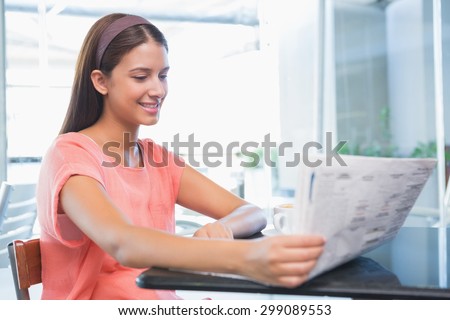 Young happy woman reading the newspaper in the cafe