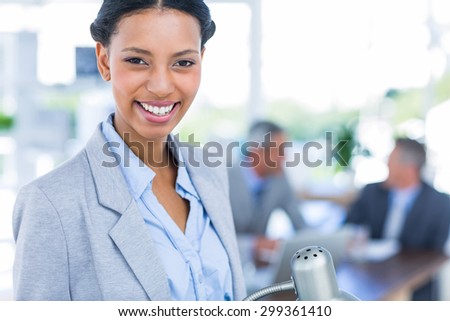 Happy businesswoman looking at camera with her colleagues behind her in office