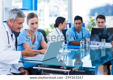 Doctor and nurse looking at laptop with colleagues behind in medical office