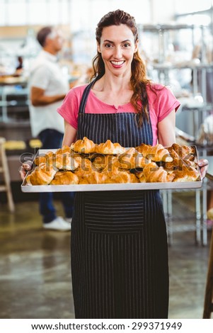 Baker showing tray of fresh croissant in the kitchen of the bakery