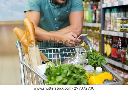 Man buy products and using his smartphone at supermarket