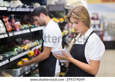 Serious staff woman wrting on notepad at supermarket