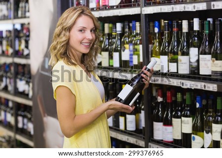 Portrait of a smiling pretty blonde woman having a wine bottle in her hands in supermarket