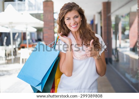 Portrait of smiling woman with shopping bags looking at camera and showing thumbs up at the shopping mall