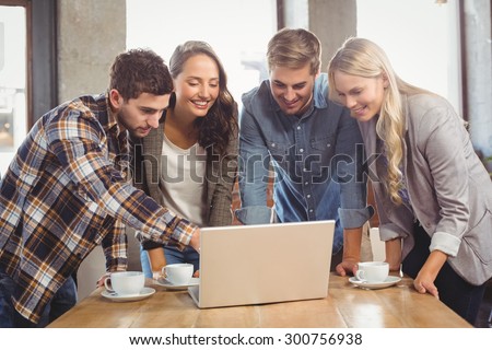 Smiling friends standing and pointing on laptop screen at coffee shop