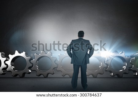 Businessman standing back to the camera with hands on hip against black wall