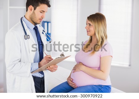Smiling pregnant patient talking to doctor which is taking notes in medical office