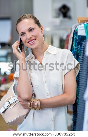 Smiling woman phoning next to clothes rail in clothing store
