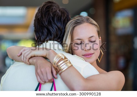 Smiling woman hugging her boyfriend with eyes closed at shopping mall