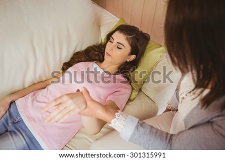 Hypnotherapist holding her patients wrist in therapists office
