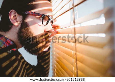 Hipster businessman peeking through blinds in his office