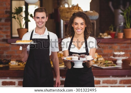 Portrait of smiling waiter and waitress showing plates with treat at coffee shop