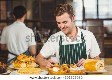 Smiling waiter tidying up the pastries at the coffee shop