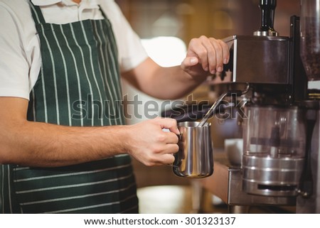 Barista steaming milk at the coffee machine at the coffee shop