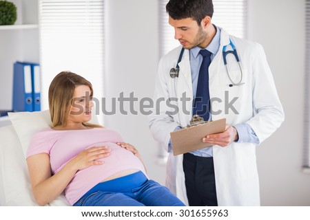 Doctor giving advice to lying pregnant patient in medical office