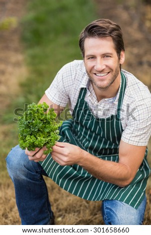 Young happy farmer looking at camera while holding vegetable in the field