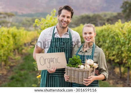 Two young happy farmers holding a sign and a basket of vegetables in the fields