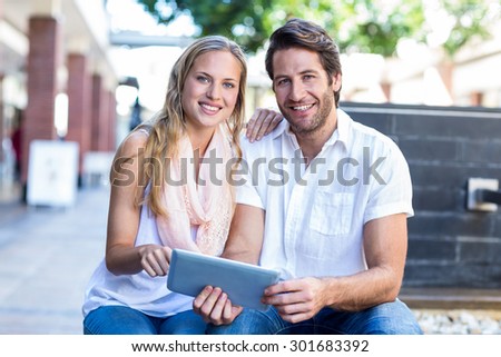 Portrait of smiling couple sitting and using tablet computer together at shopping mall