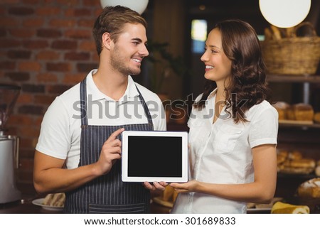 Smiling co-workers showing a tablet at the coffee shop