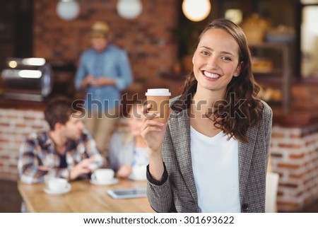 Portrait of smiling young woman with take-away cup in front of her friends at coffee shop