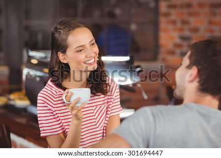 Smiling young woman enjoying coffee with a friend at coffee shop